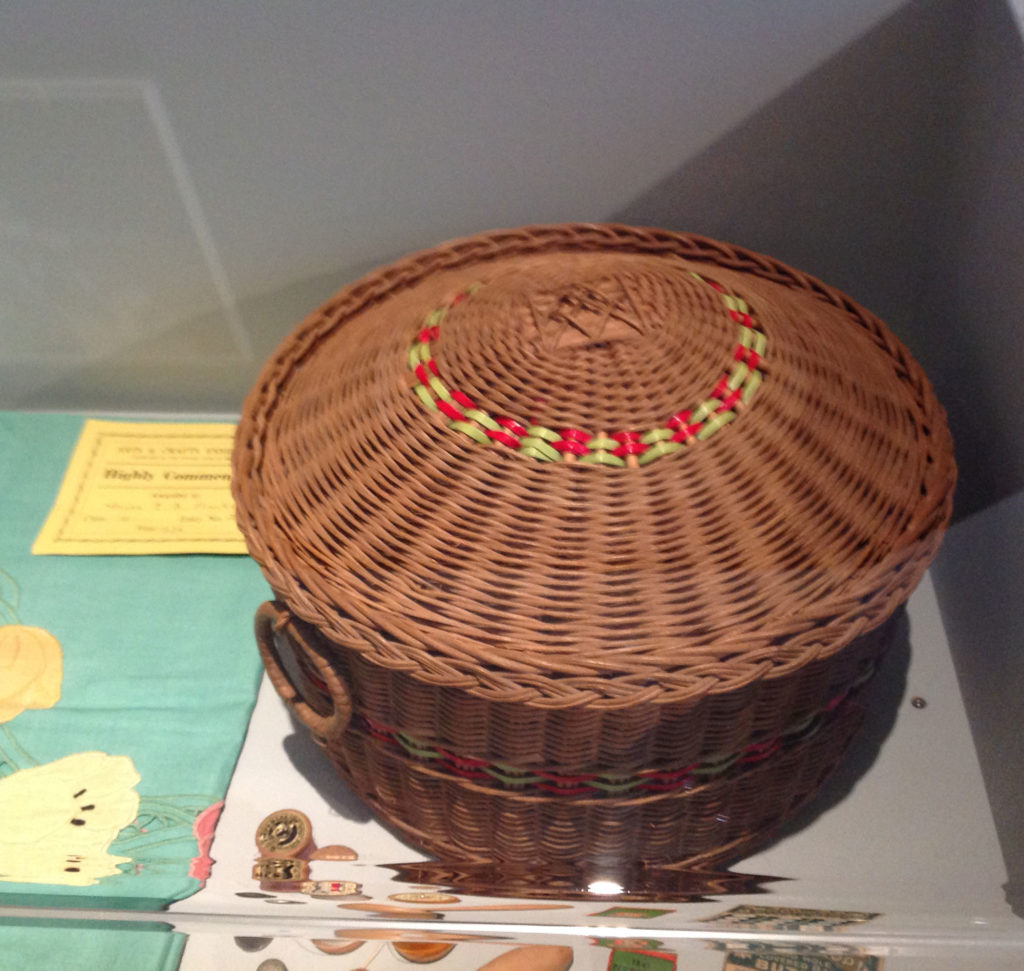 Image shows round brown basket with red and yellow decoration in the lid.