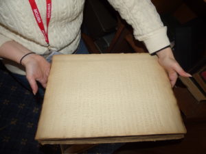 The image shows two hands holding the oversized and thick book which is about the size of a modern laptop