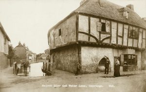 Exterior view from the north-east showing a man and woman with a boy outside the Maison Dieu house, with a horse and cart standing in the stream to the left