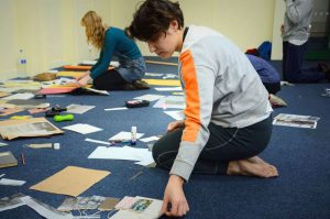 Image shows woman in jeans and barefoot kneeling on the floor assembling historic images into a presentation.