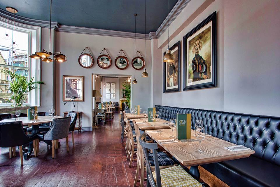 Image shows a long room with tables for restaurant meals, four round mirrors high on the wall, and paintings of dogs in 19th century upper class dress.