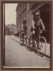 Two older scouts from the Guild on bicycles on a cobbled street