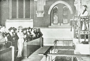 Image shows people in Victorian dress signing during a church service