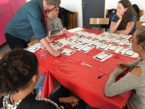 The participants are all gathered around a table and are looking at pieces of paper each with different ideas on