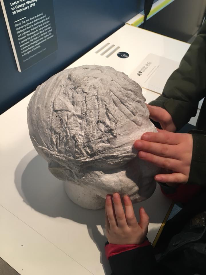 The image shows two sets of children's hands exploring the life sized bust of Edward Rushton