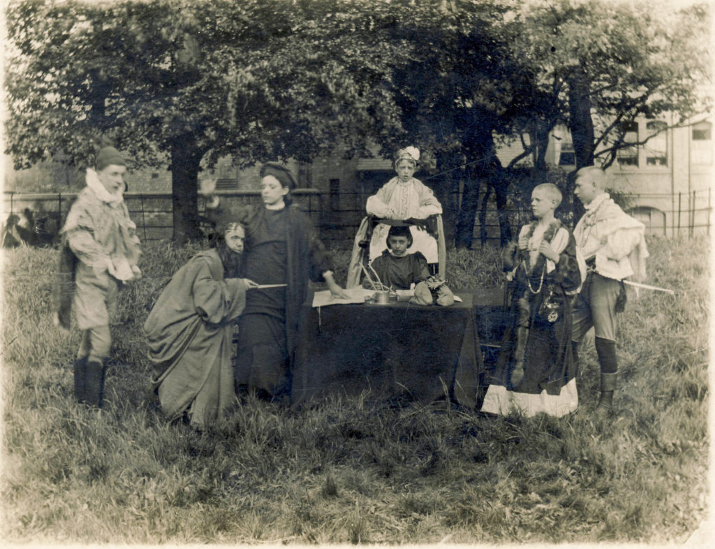 The image shows a blank and white photographs of students dressed in costumes peforming a play
