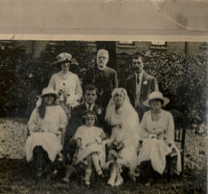 A wedding party of eight people including a bride and other women in white, a vicar and two men in suits